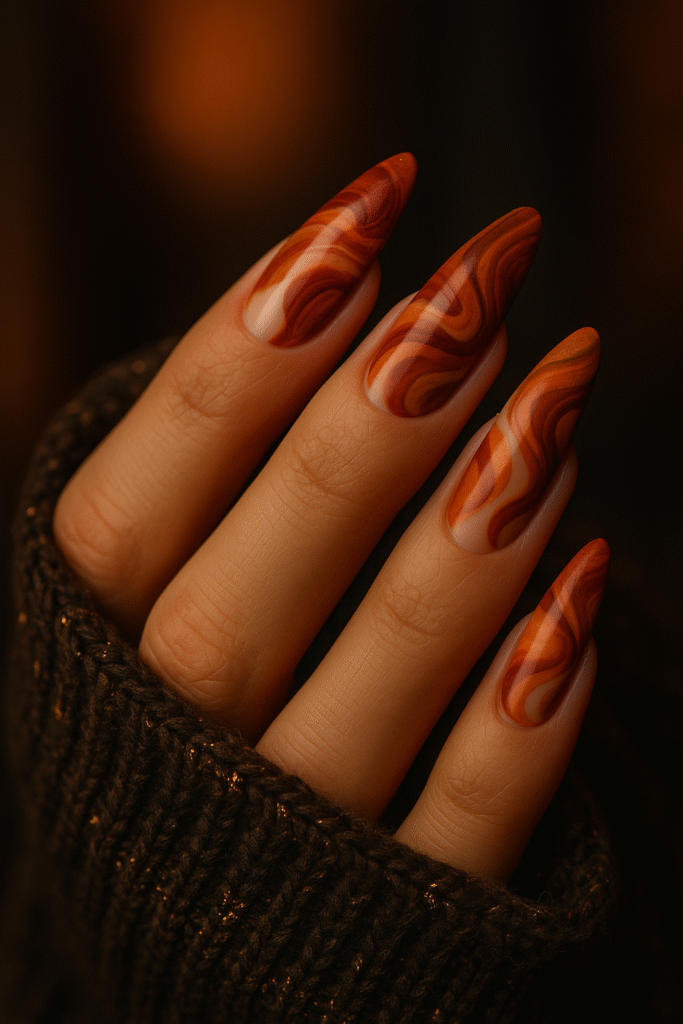 Almond nails with swirling burnt orange, rust, and clay abstract patterns with gold foil accents.