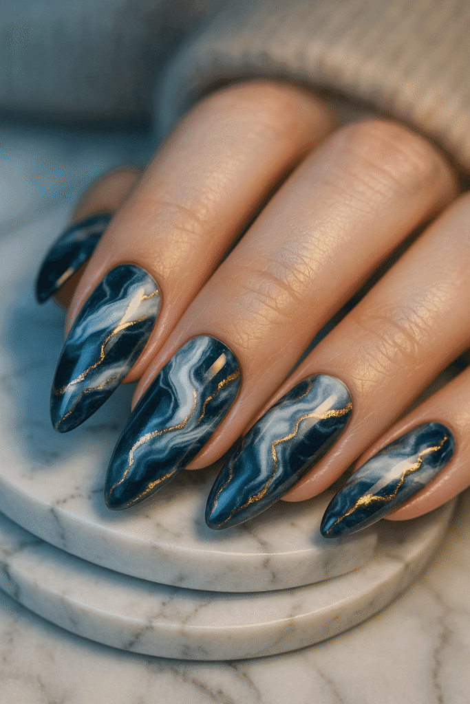 Navy marble nails with pearl white swirls and gold foil veins, glossy almond shape.